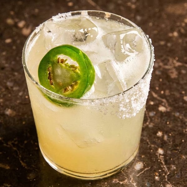 Spicy margarita with a salted rim and a jalapeño slice, on a dark marble surface.