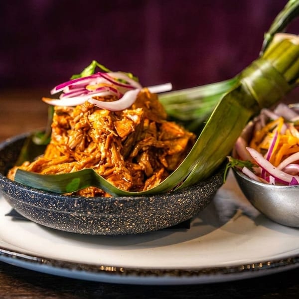 Shredded meat in a small skillet lined with a banana leaf, served with pickled onions.