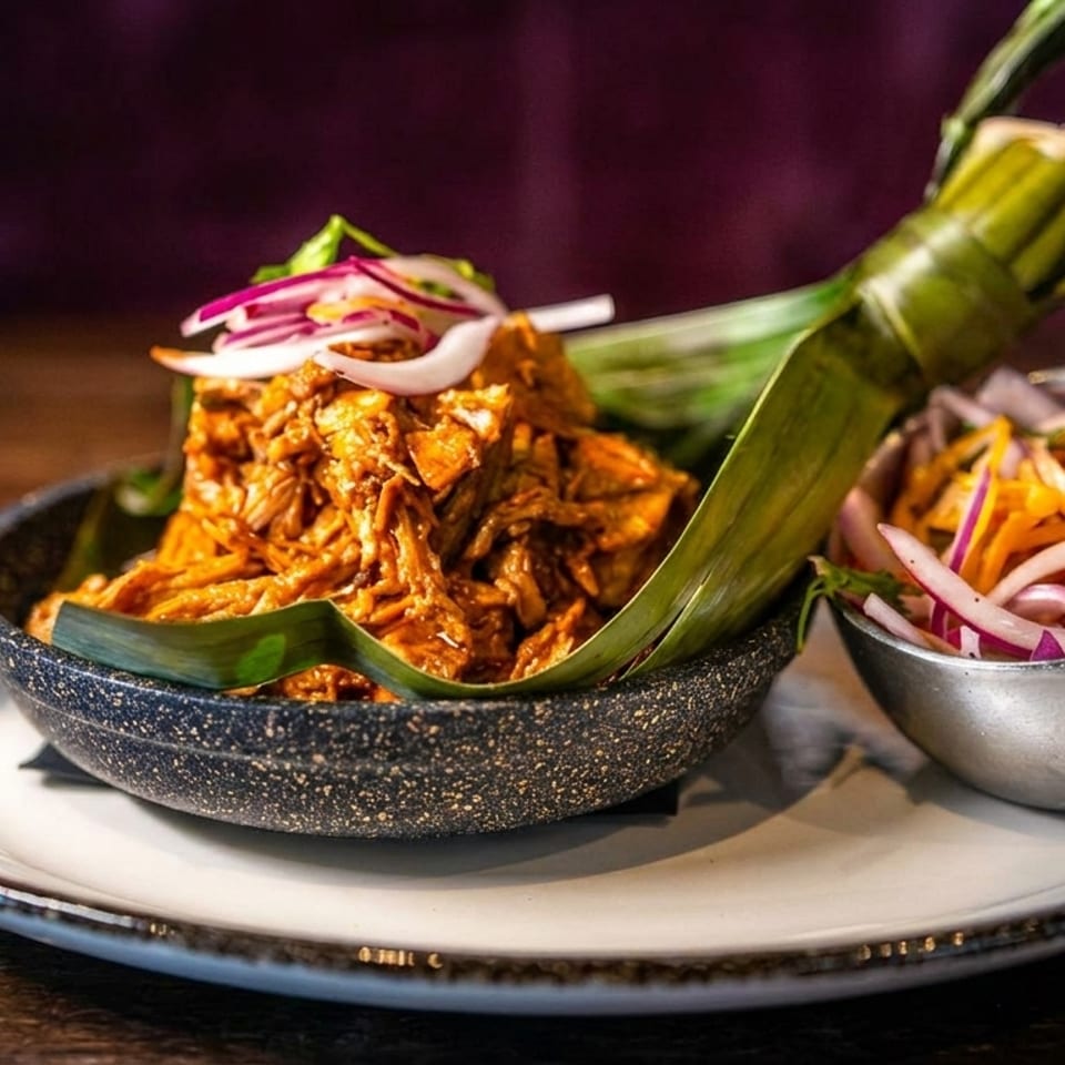 Shredded meat in a small skillet lined with a banana leaf, served with pickled onions.