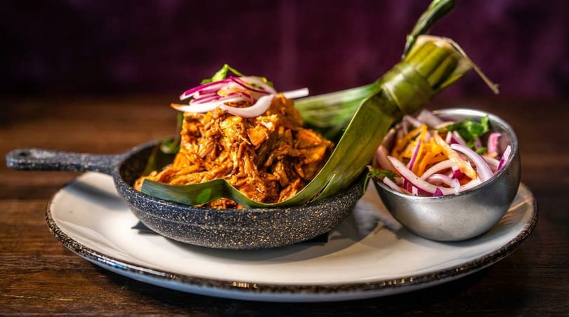 Shredded meat in a small skillet lined with a banana leaf, served with pickled onions.